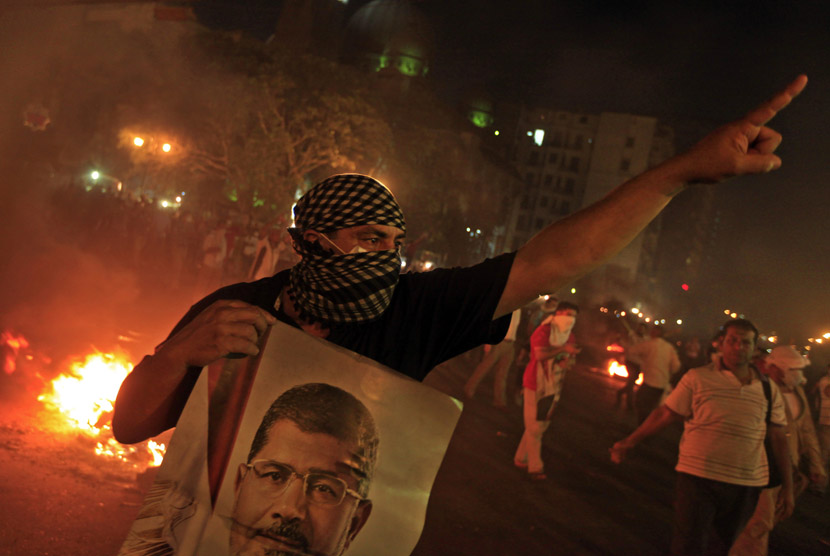 Seorang pengunjuk rasa memegang poster Presiden Mursi saat berunjuk rasa menolak kudeta militer di pusat kota Kairo, Senin (15/7).     (AP/Khalil Hamra)