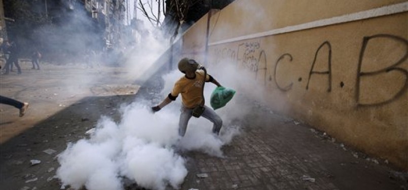 Seorang pengunjuk rasa mengenakan masker tengah melemparkan gas air mata ke dalam kantor Kementerian Dalam Negeri Mesir, Ahad (5/2).