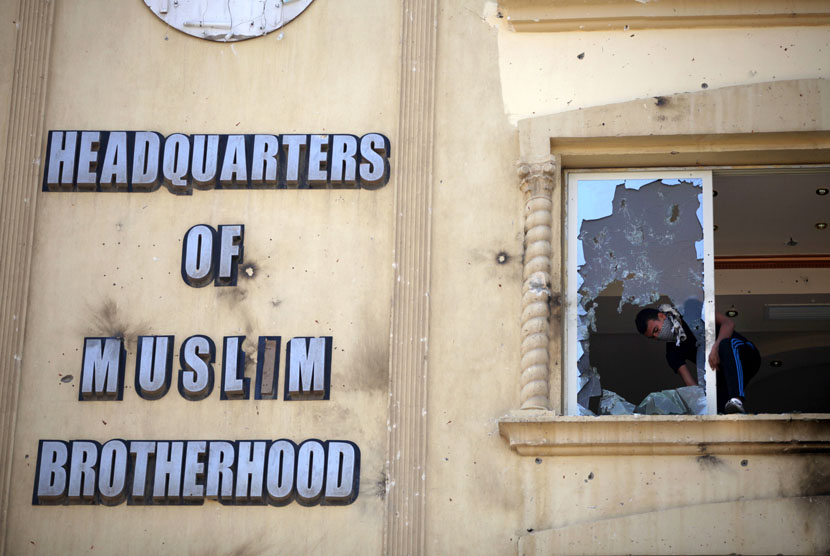 Seorang pengunjuk rasa merusak jendela markas Ikhwanul Muslimin di distrik Muqatam di Kairo, Senin (1/7).       (AP/Khalil Hamra)
