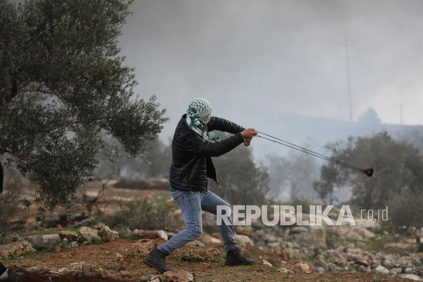  Seorang pengunjuk rasa Palestina melemparkan batu ke pasukan Israel selama demonstrasi menentang pemukiman Israel di tanah desa Beita, dekat kota Nablus, Tepi Barat, 11 Februari 2022. 