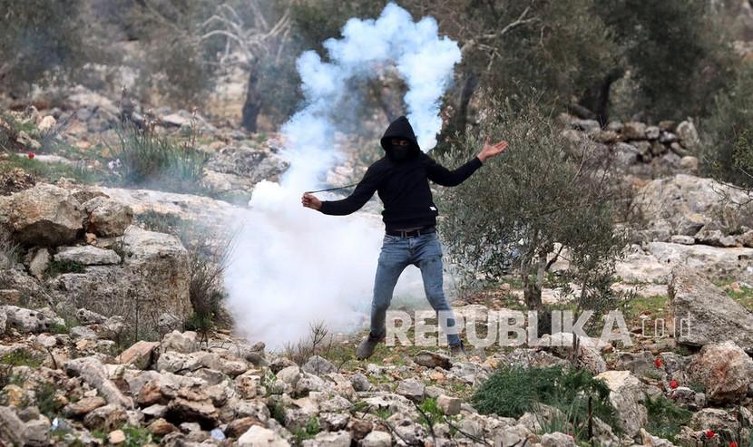  Seorang pengunjuk rasa Palestina melemparkan tabung gas air mata kembali ke pasukan Israel selama demonstrasi menentang pemukiman Israel di tanah desa Beita, dekat kota Nablus, Tepi Barat, 11 Februari 2022. 