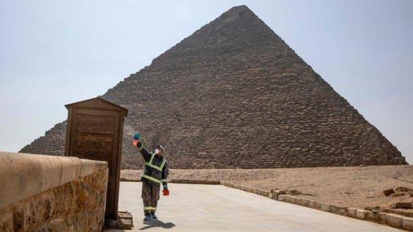 Seorang penjaga kawasan Piramida Giza menyemprotlam cariaran sanitasi untuk cegah Corona.