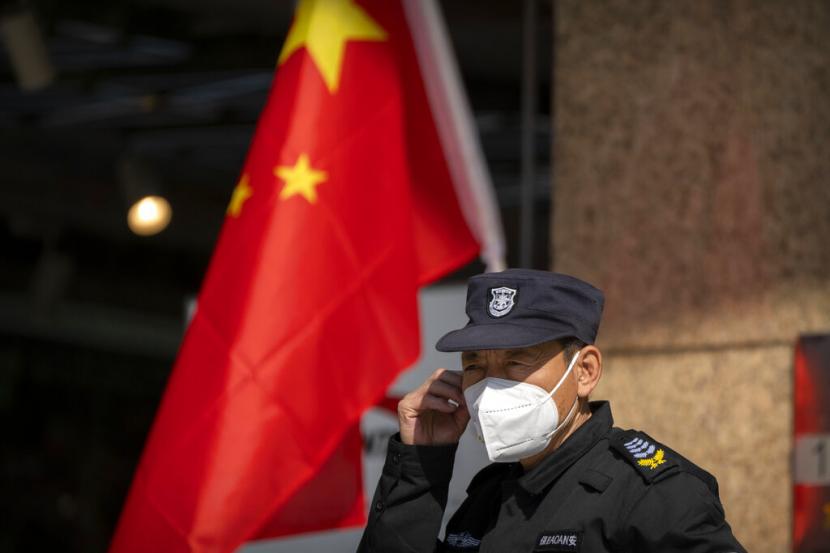 Seorang penjaga keamanan yang mengenakan masker berdiri di dekat bendera China. China jatuhkan sanksi pada dua warga AS terkait pelanggaran HAM di Tibet. Ilustrasi.