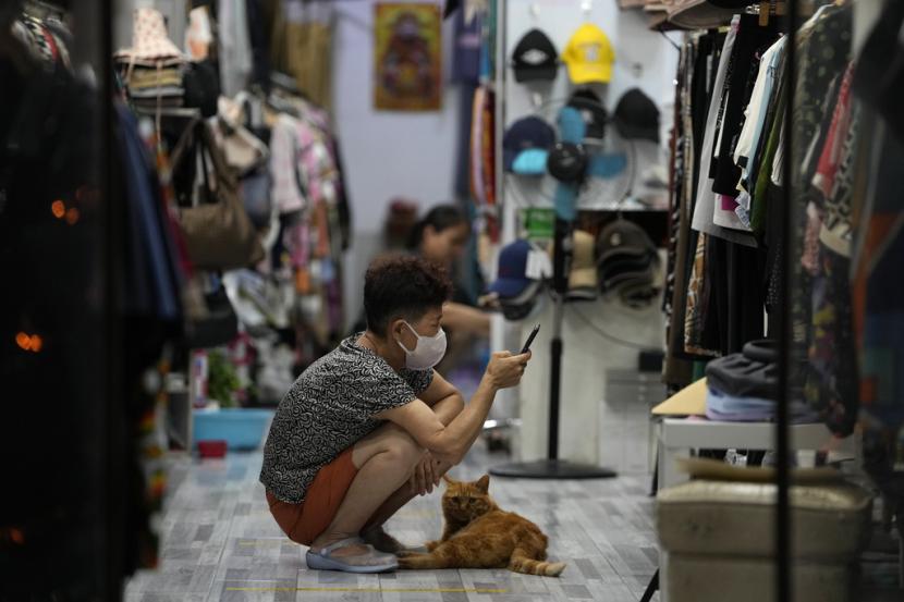 Seorang penjual menunggu dengan kucingnya untuk pelanggan di sebuah toko di Beijing, Kamis, 27 Juli 2023. Perencana ekonomi terkemuka China pada Selasa (1/8/2023) meluncurkan serangkaian langkah terperinci termasuk pengurangan pajak.