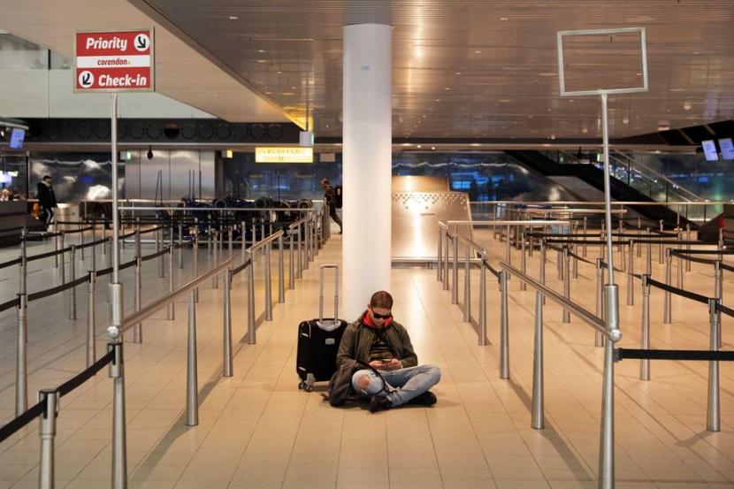 Seorang penumpang duduk di lantai Bandara Schipol, Belanda pada Jumat (13/3). Pemerintah Belanda memerintahkan semua sekolah, restoran, dan klub olahraga ditutup sebagai bentuk pengetatan langkah pencegahan wabah corona.  