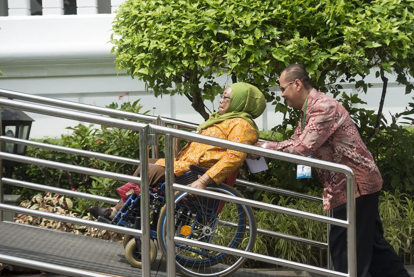 Seorang penyandang disabilitas netra (kanan) membantu mendorong kursi roda yang dinaiki oleh seorang penyandang disabilitas tubuh ketika berjalan memasuki Istana Negara melalui jalur khusus untuk menghadiri acara puncak peringatan Hari Disabilitas Internas