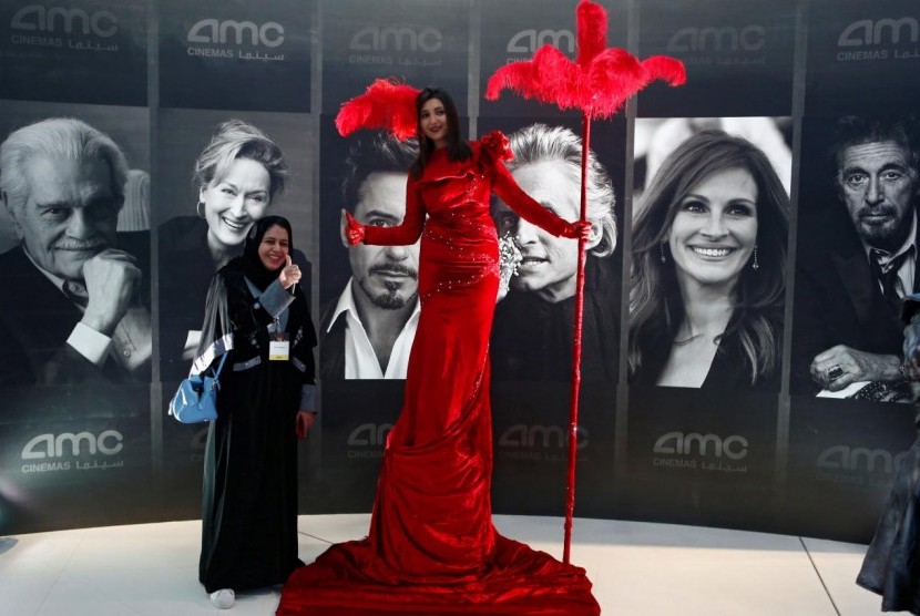 Seorang perempuan Arab Saudi berpose di depan bioskop komersil pertama yang dibuka negara tersebut. Jaringan Sinema Terbesar di Dunia AMC Tarik Diri dari Pasar Arab Saudi