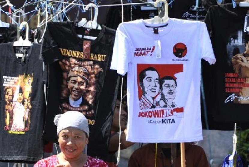 Seorang perempuan berdiri di depan kios kaki lima yang menjual kaos bergambar Jokowi-JK adalah Kita di Surabaya, Jawa Timur, Ahad (29/6). 