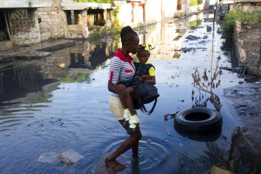 Seorang perempuan berjalan di jalanan yang penuh kotoran saat ia menggendong putrinya ke sekolah di daerah kumuh Cite Soleil di Port-au-Prince, Haiti. Foto diambil pada Rabu (3/10).