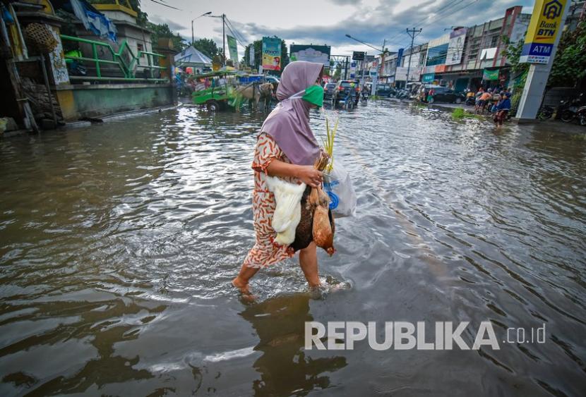 Seorang perempuan berjalan melintasi genangan air di jalan Pasar Kebon Roek, Ampenan, Kota Mataram, Provinsi Nusa Tenggara Barat (NTB), Jumat (29/5/2020).