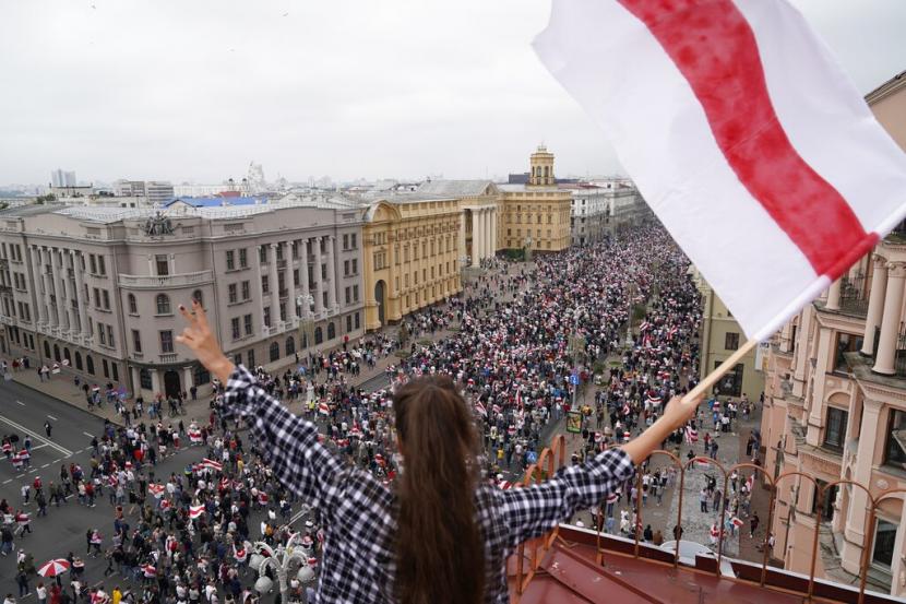 Seorang perempuan membawa bendera Belarus berdiri di atap sebuah bangunan di Minsk, Ahad (23/8). 