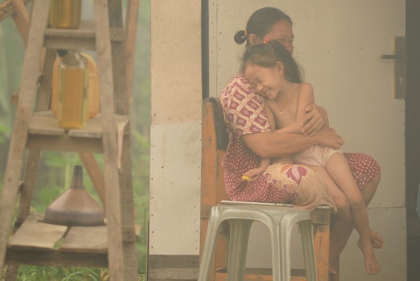 Seorang perempuan memeluk bocah di depan rumahnya yang diselimuti kabut asap tebal di Jalan S Parman, Palangkaraya, Kalimantan Tengah, Selasa (27/10). 