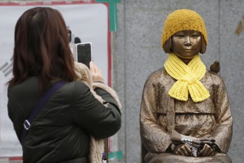 Seorang perempuan mengambil gambar patung seorang gadis yang melambangkan korban budak seks Jepang saat PD II di depan Kedubes Jepang di Seoul, Korsel, Selasa, 29 Desember 2015.