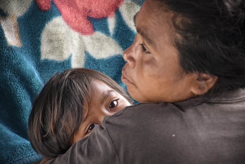 Seorang perempuan mengendong anaknya di tenda perawatan pascagempa di Desa Sembalun Bumbung, Kecamatan Sembalun, Selong, Lombok Timur, NTB. Gempa bumi 6,4 Skala Richter (SR) mengguncang wilayah Lombok, Nusa Tenggara Barat, Ahad (29/7).