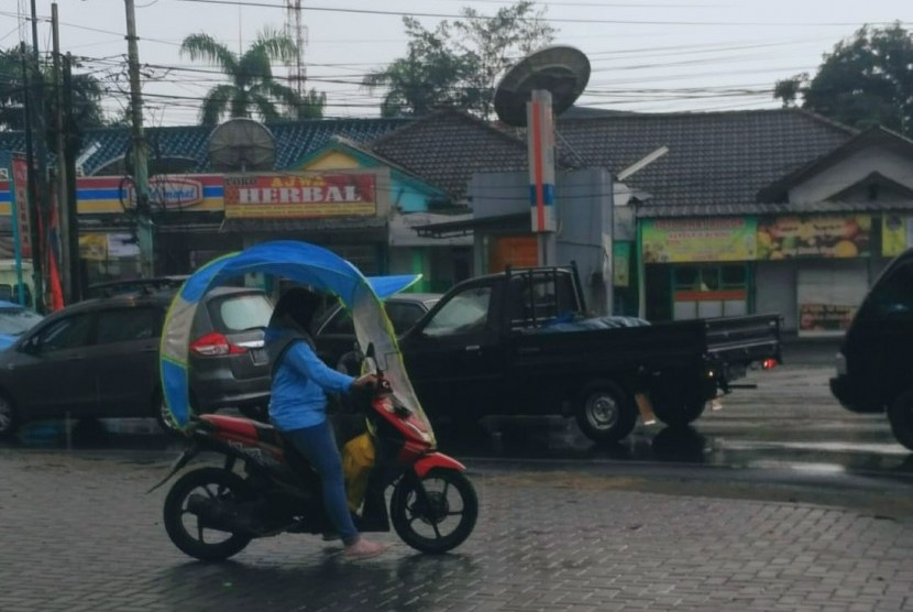 Seorang perempuan menggunakan mantel hujan untuk motor melintas di kawasan Sawangan, Depok. Pelebaran Jalan Raya Sawangan dilakukan untuk mengatasi kemacetan. Ilustrasi.