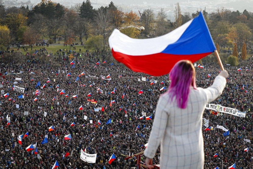 Seorang perempuan mengibarkan bendera Ceska dari atap saat demonstrasi menuntut Perdana Menteri Andrej Babis mundur di Praha, Ceska, Sabtu (16/11).