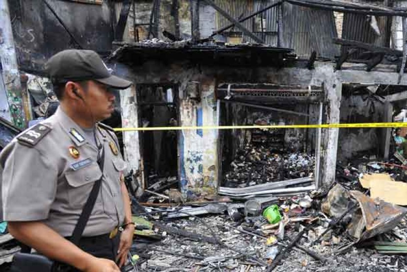 Seorang personel kepolisian melintasi bangunan yang terbakar akibat tawuran antarwarga di Johar Baru, Jakarta Pusat, Senin (18/11).