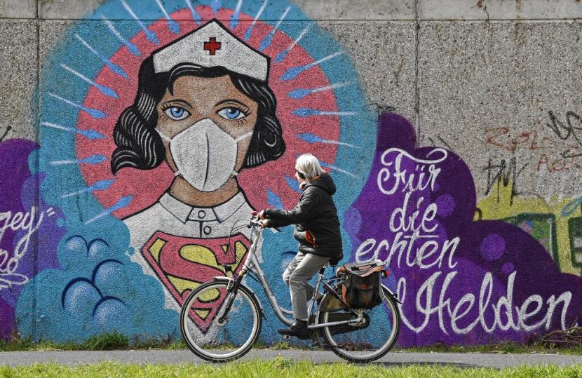 Seorang pesepeda melintasi grafiti yang menggambarkan seorang superhero berpakaian perawat dengan tulisan yang berarti 