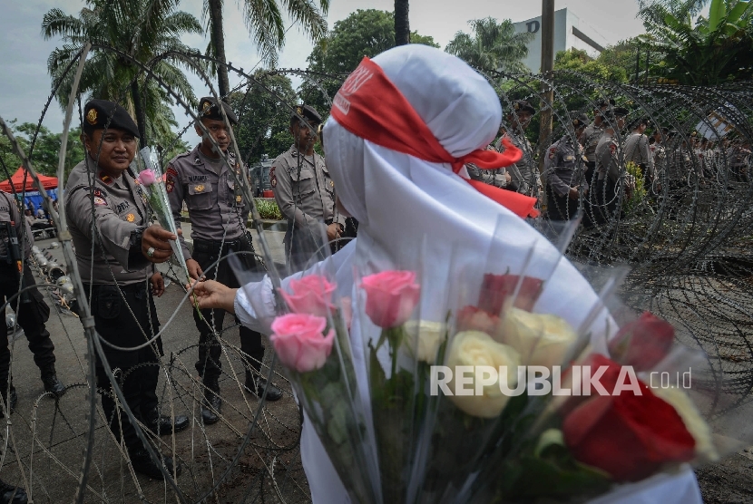 Seorang peserta aksi yang tergabung dalam Gerakan Nasional Pengawal Fatwa (GNPF) MUI memberikan bunga kepada anggota kepolisian di depan pagar berduri saat sidang penistaan agama berlangsung di auditorium Kementerian Pertanian, Jakarta Selatan, Selasa (10/1).