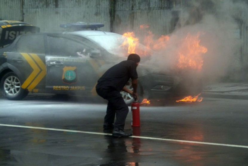 Seorang petugas berusaha memadamkan api yang membakar mobil polisi di Jalan Gunung Sahari, Jakarta Pusat, Jumat ( 18/1).