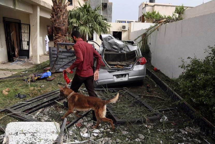   Seorang petugas keamanan menggunakan anjing pelacak memeriksa  lokasi ledakan sebuah bom mobil yang menargetkan Kedubes Perancis di Tripoli, Libya, Selasa (23/4).      (AP/Abdul Majeed Forjani)