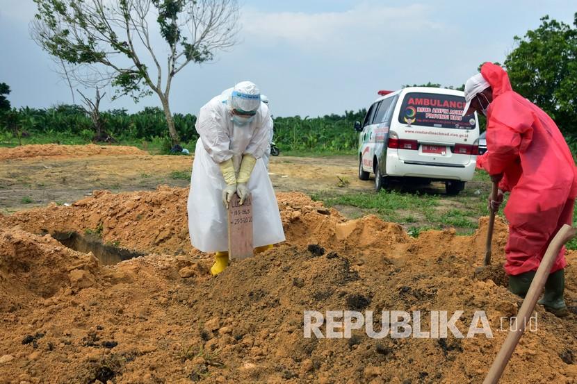 Seorang petugas kesehatan (kiri) mengenakan alat pelindung diri saat menancapkan nisan pada makam jenazah yang dikuburkan dengan protokol kesehatan Covid-19. Tiga PDP dengan hasil rapid test non reaktif meninggal dunia di Ogan Komering Ulu Selatan, Sumatra Selatan. 