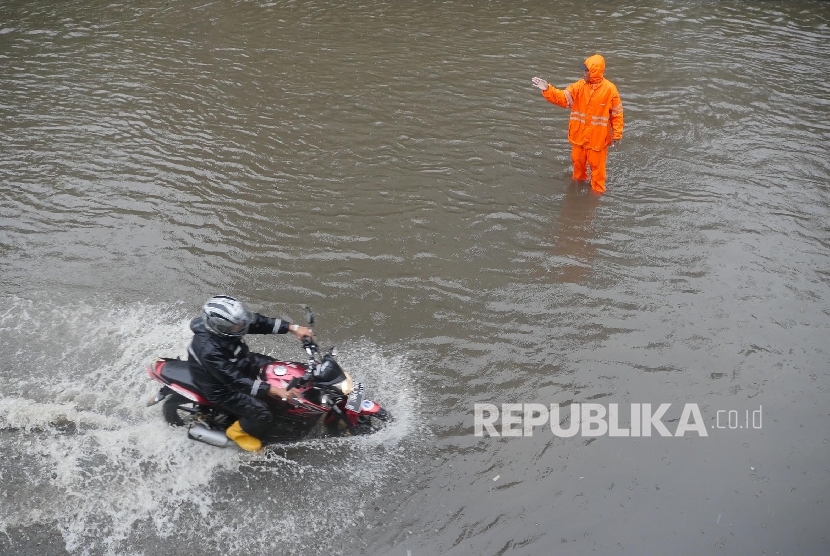 Seorang petugas memberikan arahan kepada pengguna jalan agar mengikuti arahannya saat melintas di kisaran jalan landas pacu timur kemayoran, Jakarta, yang digenangi air, Selasa (21/2)