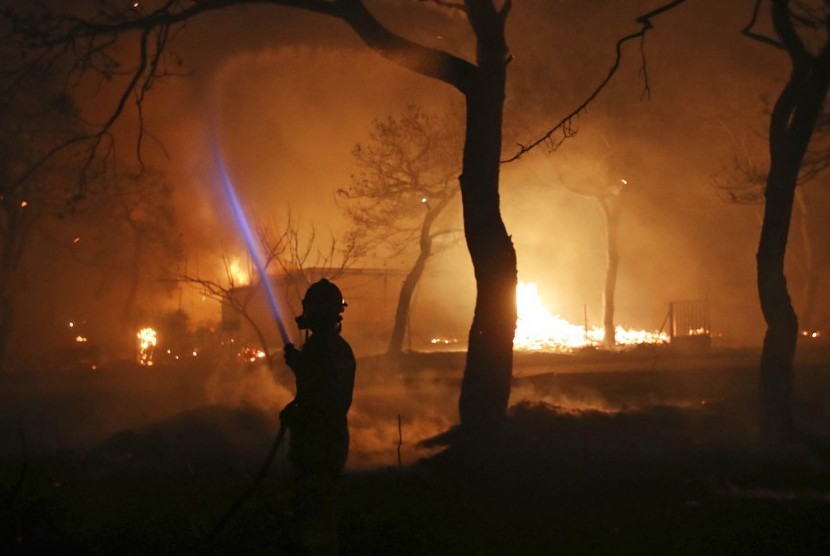 Seorang petugas pemadam kebakaran menyemprotkan air ke lokasi kebakaran di timur Athena, Senin (23/7).