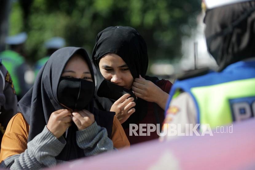 Seorang petugas polisi membagikan dan meminta pengendara untuk memakai masker pelindung selama kampanye protokol kesehatan (ilustrasi)