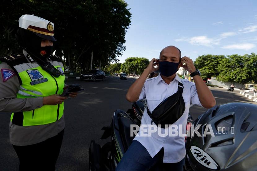 Seorang petugas polisi membagikan dan meminta pengendara untuk memakai masker pelindung selama kampanye protokol kesehatan di Banda Aceh (19/8/2020). 