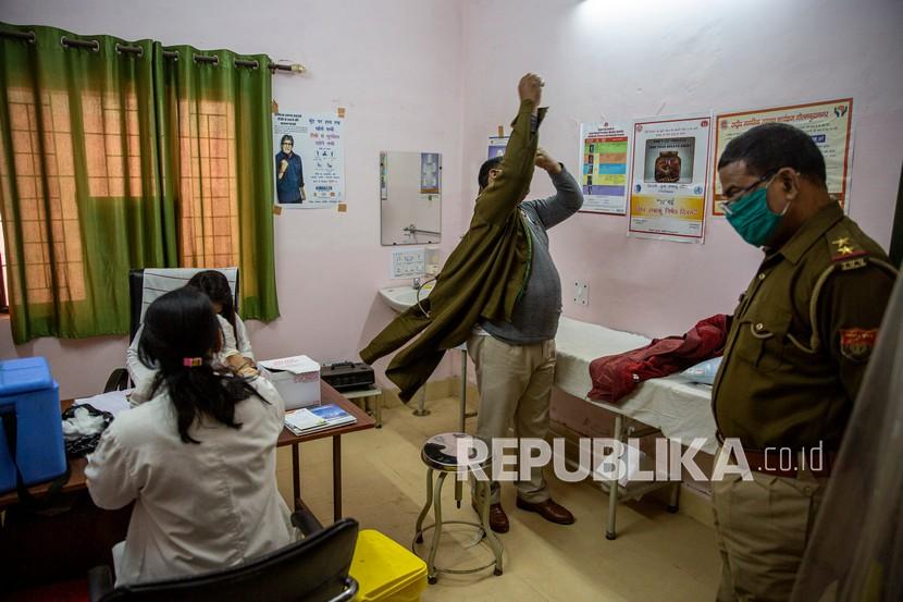 Seorang petugas polisi mengenakan seragamnya setelah menerima vaksin COVID-19 sementara rekannya menunggu gilirannya di sebuah pusat kesehatan di Greater Noida, pinggiran kota New Delhi, India, Kamis (11/2).
