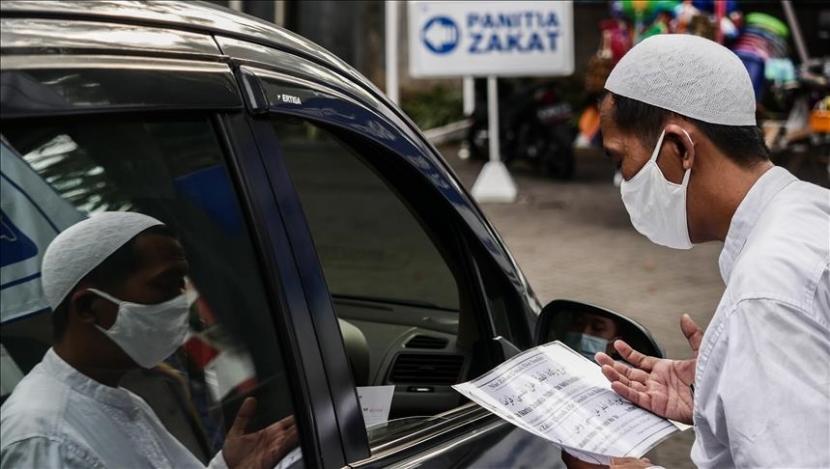 Seorang petugas zakat menggunakan masker berdoa saat menerima pembayaran zakat fitrah pada bulan suci Ramadhan dengan sistem drive-thru sebagai langkah-langkah pencegahan penyebaran virus corona (Covid-19) di Masjid Al-Azhar di Jakarta, Indonesia, pada 21 Mei, 2020.