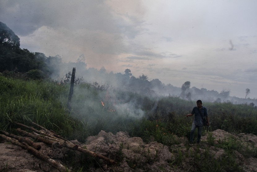 Seorang pewarta foto berlari menghindari kepulan asap saat mengabadikan kebakaran lahan di Pekanbaru, Riau, Rabu (11/1).