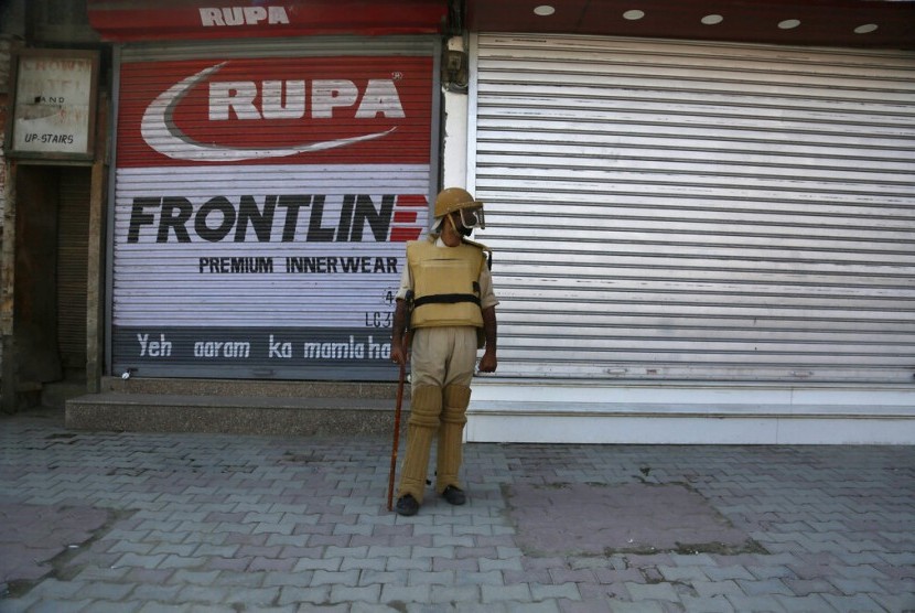 Seorang polisi Kashmir berjaga di luar sebuah toko yang tutup di Srinagar, Kashmir yang dikuasai India.