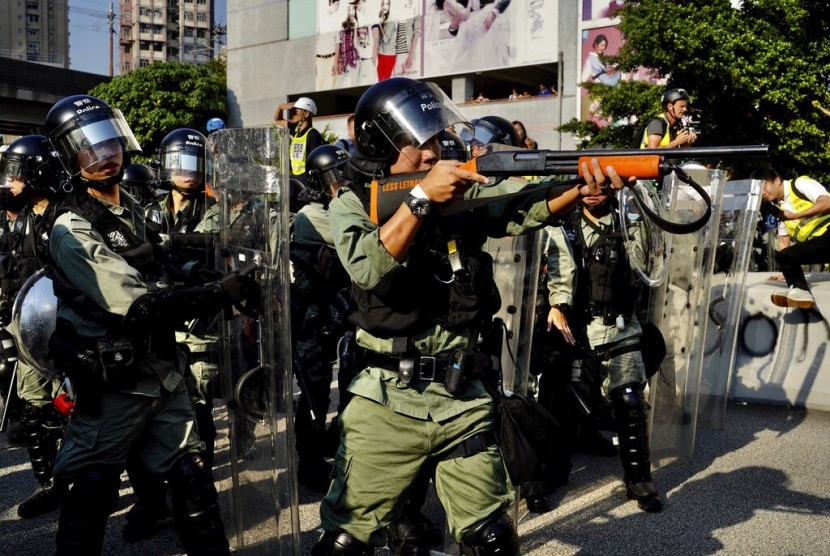 Seorang polisi mengacungkan senjata pengendali kerumunan ke arah demonstran di Hong Kong.
