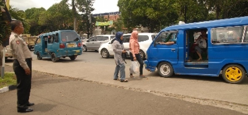 Seorang polisi mengawasi dua penumpang wanita menaiki angkot di depan Mapolresta Depok, Jawa Barat, Jumat (16/12).