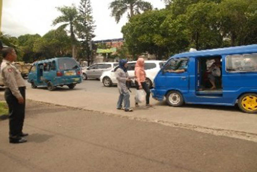 Seorang polisi mengawasi dua penumpang wanita menaiki angkot di depan Mapolresta Depok, Jawa Barat.