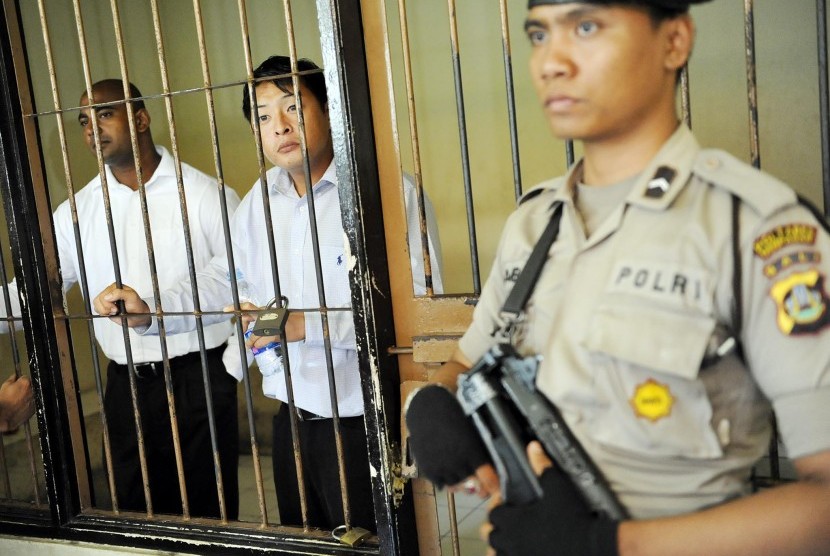 Seorang polisi menjaga dua warga Australia terpidana mati dalam kasus penyelundupan 8,2kg heroin Andrew Chan (tengah) dan Myuran Sukumaran (kiri) saat akan menghadiri sidang peninjauan kembali (PK) di Pengadilan Negeri Denpasar, Bali, dalam foto arsip bert