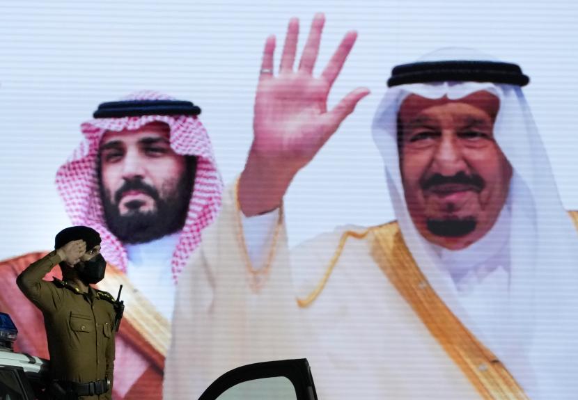 Seorang polisi Saudi memberi hormat di depan layar yang menampilkan gambar Raja Saudi Salman, kanan, dan Putra Mahkota Mohammed bin Salman setelah parade militer dalam persiapan untuk ziarah haji tahunan, di kota suci Muslim Mekah, Arab Saudi, Ahad, Juli 3, 2022. 