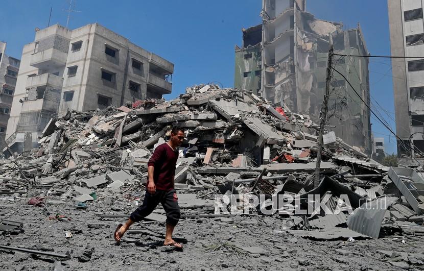 Seorang pria berjalan melewati puing-puing bangunan perumahan Yazegi yang dihancurkan oleh serangan udara Israel, di Kota Gaza, Ahad (16/5).