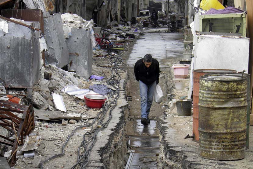   Seorang pria berjalan sambil menundukkan kepala, menghindari bidikan penembak jitu pasukan pendukung Presiden Bashar di kota Homs, Suriah, Ahad (9/3).  (Reuters/Thaer Al Khalidiya)