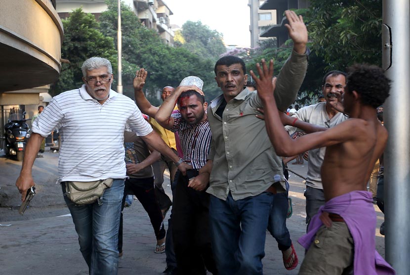 Seorang pria berpakaian sipil membawa senpi (kiri) menahan seorang pendukung Presiden Muhammad Mursi yang terluka dalam bentrokan yang terjadi di Kairo, Mesir, Senin (22/7).      (AP/ Hussein Malla)