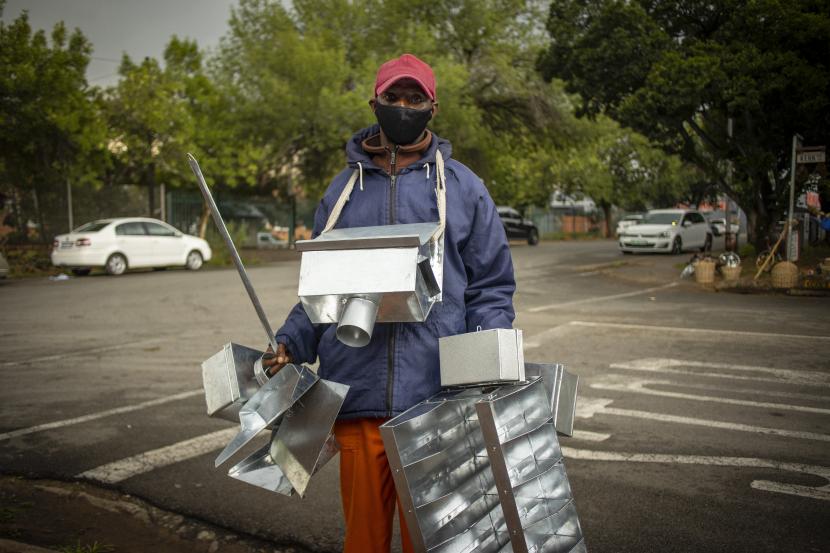 Seorang pria bertopeng yang menjual kerajinan logam buatan tangan berjalan melalui jalan-jalan di kota pedesaan Parys, Afrika Selatan, 26 November 2021. Kemunculan varian Omicron mengancam kelangsungan industri pariwisata Afrika Selatan. Ilustrasi.