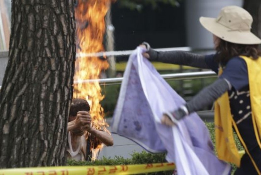 Seorang pria Korea Selatan (kiri) membakar diri di depan Kedutaan Jepang di Seoul (kiri), sementara seorang perempuan berupaya memadamkan api (12/8).