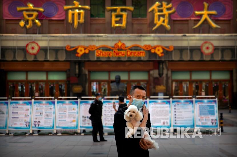 Seorang pria memakai masker untuk mencegah penyebaran virus Corona saat menggendong seekor anjing ketika melintasi di sepanjang jalan perbelanjaan Kota Wuhan di China.