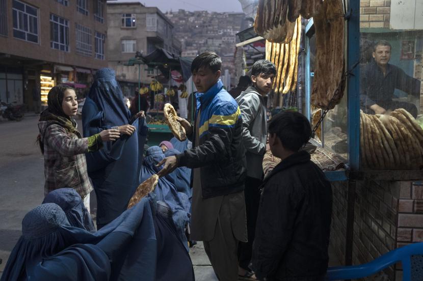 Seorang pria membagikan roti kepada wanita Afghanistan yang mengenakan Burka di luar sebuah toko roti di Kabul, Afghanistan. Sekitar 258 juta orang di 58 negara menghadapi 