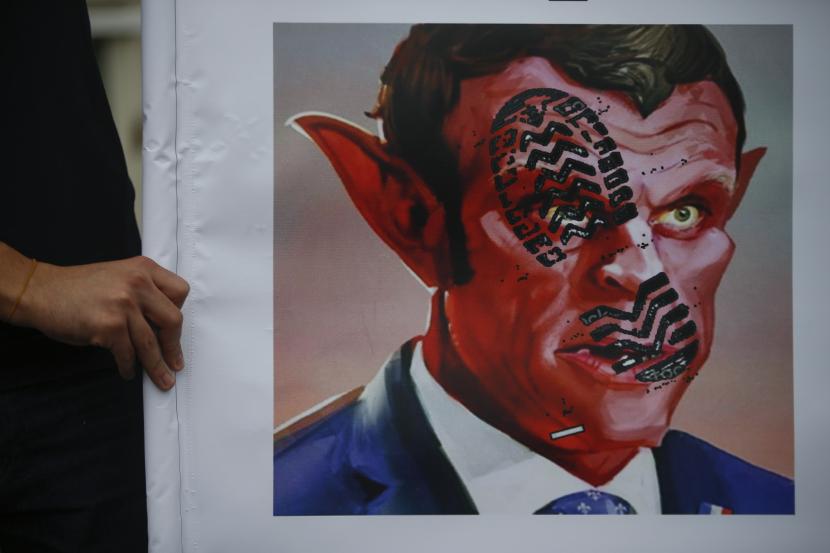  Seorang pria memegang poster karikatur Presiden Prancis Emmanuel Macron, yang menggambarkan dia sebagai setan saat melakukan protes terhadap Prancis di Istanbul, (ilustrasi).