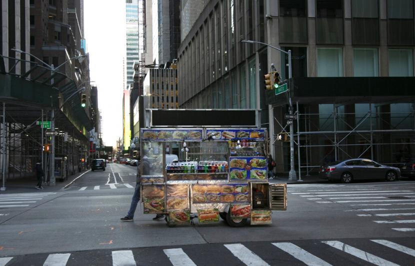 Seorang pria menarik gerai makanannya melewati jalanan yang sepi dekat Times Square, New York, Senin (16/3) waktu Indonesia. Wali Kota New York mengumumkan penutupan restoran dan tempat publik lainnya akibat merebaknya virus corona jenis baru. 