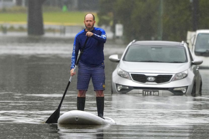 Seorang pria mendayung di papan dayung melalui jalan banjir.