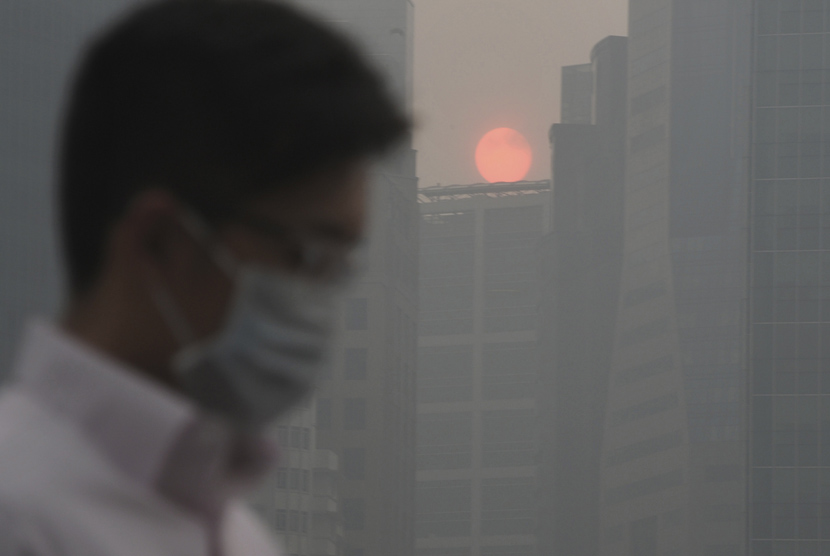 Seorang pria mengenakan masker berjalan saat matahari terbenam di antara bangunan yang tertutup kabut di kawasan pusat bisnis Singapura,Kamis (20/6).    (AP/Joseph Nair)